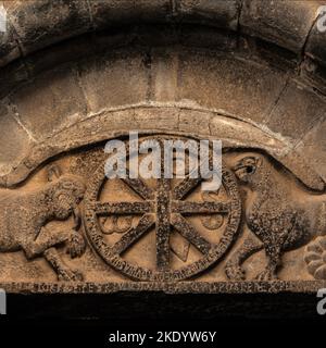 Knurrende Löwen und christliche Symbole. Geformtes romanisches Tympanum über dem nördlichen Portal der ehemaligen königlichen Klosterkirche Santa Maria in Santa Cruz de la Serós in Huesca, Aragon, Spanien. Die Kirche, die erstmals im Jahr 1070 erwähnt wurde, wurde für ein Benediktinerkloster errichtet, das vom Königshaus Aragonien als „Familienkloster“ gegründet wurde. Das Tympanum ist auch mit einer lateinischen Inschrift versehen, die die Gläubigen auffordert, „diesen gesegneten Tempel der Jungfrau“ zu betreten. Stockfoto