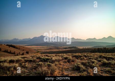 Die Sawtooth Mountain Range von den Ausläufern nördlich von Stanley, Idaho, an einem Sommerabend gesehen. Der Himmel ist durch Waldbrandrauch trübe. Stockfoto