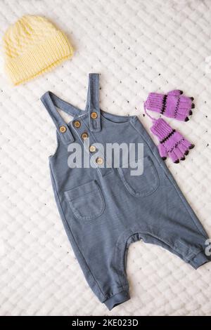 Eleganter Jumpsuit mit Strapsmütze und Handschuhen für ein Baby auf einer weißen, weichen Decke Stockfoto