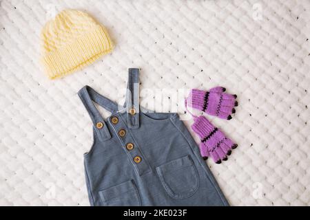 Eleganter Jumpsuit mit Strapsmütze und Handschuhen für ein Baby auf einer weißen, weichen Decke Stockfoto