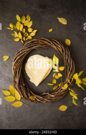 Gestrickter gelber Hut in einem Kranz aus Ästen mit gelben Blättern Stockfoto