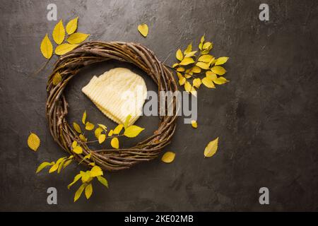 Gestrickter gelber Hut in einem Kranz aus Ästen mit gelben Blättern Stockfoto