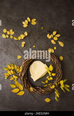 Gestrickter gelber Hut in einem Kranz aus Ästen mit gelben Blättern Stockfoto