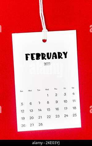 Kalenderseite Februar 2023 für 2023 Jahre an weißem Seil auf rotem Hintergrund gehängt. Stockfoto