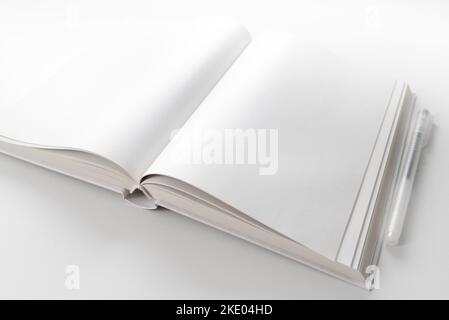 Hochwinkelige Ansicht eines offenen Buches mit leeren weißen Seiten auf weißem Schreibtisch mit Stift Stockfoto