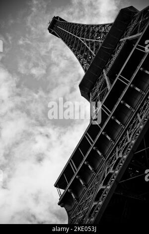 Eine vertikale Graustufenaufnahme des Eiffelturms von unten gegen bewölkten Himmel Stockfoto