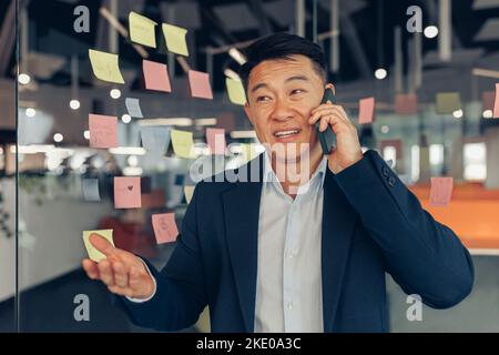 Geschäftiger asiatischer Geschäftsmann im Anzug, der im modernen Coworking telefoniert Stockfoto