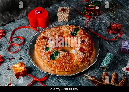 Ein Roscon de reyes, der spanische Königskuchen, der traditionell an einem epiphany Tag gegessen wird, wird auf einem silbernen Teller serviert, der auf einem grauen rustikalen Tisch neben einem ch serviert wird Stockfoto