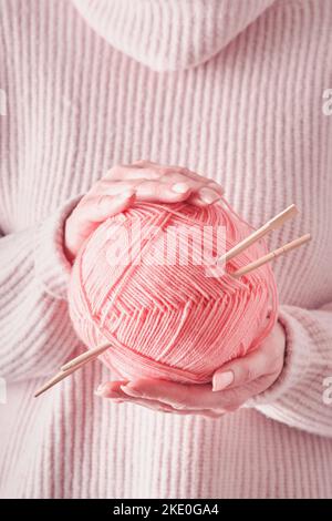 Weibliche Hände mit bunten rosa Wollgarnen und hölzernen Stricknadeln für Hobby- oder Kunstarbeiten auf blauem Hintergrund. Nadelarbeit oder Strickkonzept. Cl Stockfoto