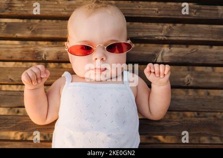 Draufsicht auf einen glücklichen kleinen Jungen mit einer Brille, die auf einer hölzernen Sonnenliege liegt Stockfoto