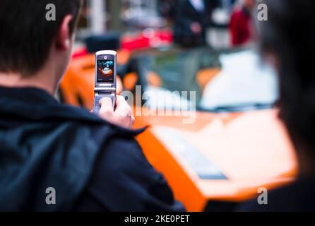 Ein junger Mann macht ein Foto mit seinem Telefon eines 2006 orangefarbenen Lamborghini Gallardo Spyder Stockfoto