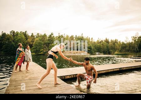 Eine Frau, die einem Freund während des Urlaubs auf dem Steg am See half Stockfoto