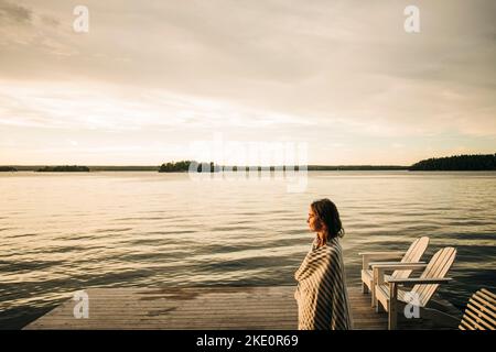 Seitenansicht einer Frau, die bei Sonnenuntergang ein Handtuch trug, während sie auf dem Steg stand Stockfoto