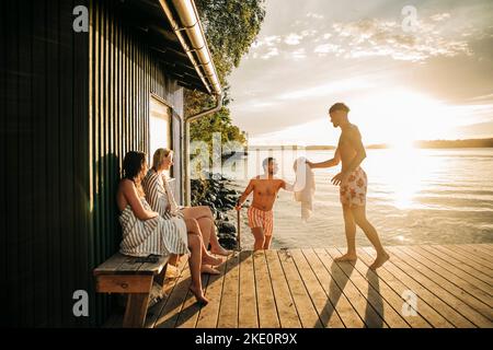 Junge Freunde genießen ihren Urlaub am Steg während des Sonnenuntergangs Stockfoto