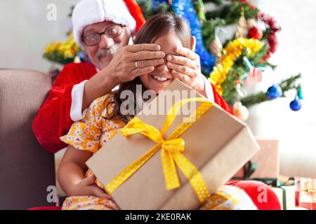 Großvater spielt am Weihnachtstag mit seiner Enkelin. Geschenke und lustige Momente. Stockfoto