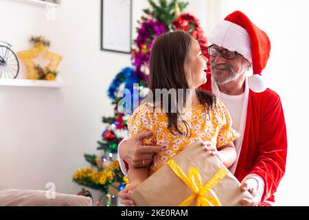 Sehr glückliches Mädchen, das ein Geschenk von ihrem Großvater als Weihnachtsmann gekleidet erhält. Weihnachtszeit zu Hause. Platz für Text. Stockfoto