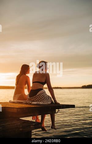 Frauen sitzen auf dem Steg am See während des Sonnenuntergangs Stockfoto