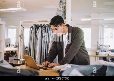 Konzentrierter männlicher Modedesigner mit Laptop in der Werkstatt Stockfoto