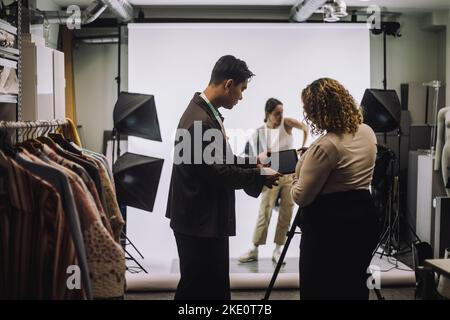Seitenansicht eines männlichen Designers, der im Studio mit einer Fotografin diskutiert Stockfoto