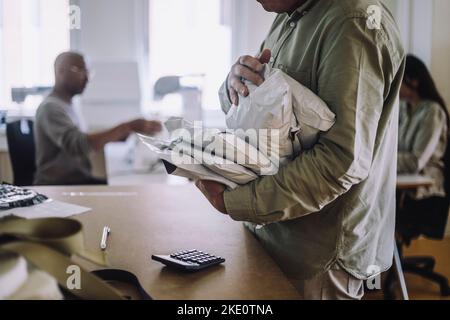 Mittelteil des männlichen Designprofi, der Pakete in der Werkstatt untersucht Stockfoto