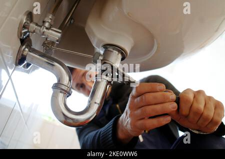 Nahaufnahme des Spülbecken für die Installierung des Installers. Männliches professionelles Reparaturgerät an der Wand im Badezimmer. Er arbeitet zu Hause an Geräten mit metallischem Werkzeug. Stockfoto