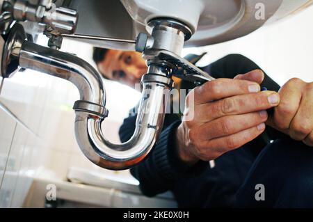 Nahaufnahme des Klempners, der die Spüle repariert. Männlicher Arbeiter, der ein Werkzeug verwendet, während er das Gerät im Badezimmer fixiert. Er arbeitet zu Hause an metallischen Geräten. Stockfoto
