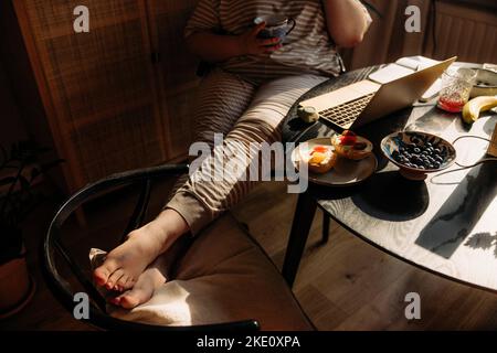 Niedriger Abschnitt der jungen Frau mit Kaffeebecher sitzen am Tisch zu Hause Stockfoto