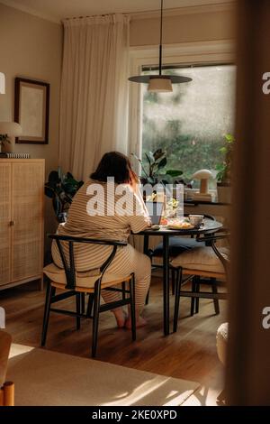 Rückansicht einer jungen Frau, die zu Hause mit einem Laptop auf einem Stuhl sitzt Stockfoto