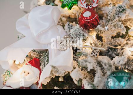 Weißer schneebedeckter Weihnachtsbaum mit Vintage-Schlüssel, Spielzeug, Bänder, Kugeln, Girlanden auf Fichtenzweigen mit Kunstschnee, Kopierraum Stockfoto
