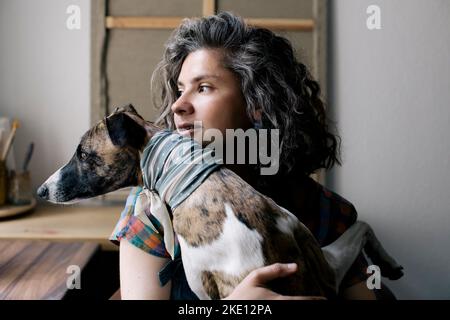 Frau schaut weg, während sie zu Hause mit Hund sitzt Stockfoto