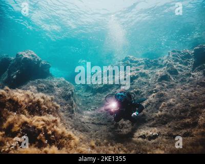 Ein Tauchgang, der von Korallen umgeben ist und die Unterwasserriffe mit einer Taschenlampe erkundet Stockfoto