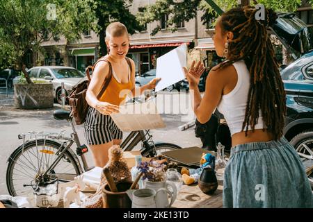 Weibliche Besitzerin, die mit Kunden kommuniziert, die beim Einkaufen auf dem Flohmarkt Platten halten Stockfoto