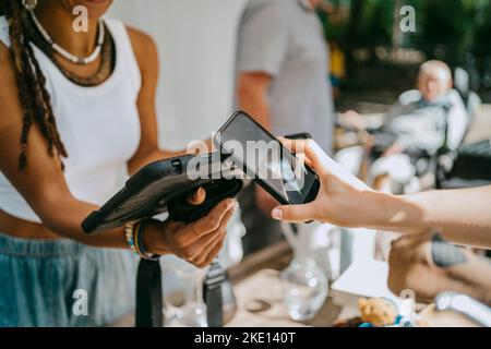 Hand einer Frau, die kontaktlos bezahlt, während sie auf dem Flohmarkt einkaufen Stockfoto