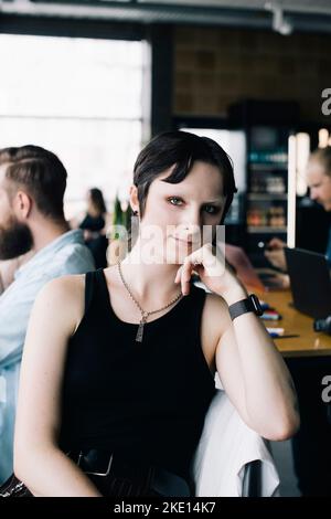 Porträt eines selbstbewussten nicht-binären Programmierers mit der Hand am Kinn im Büro Stockfoto