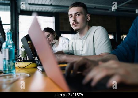 Porträt eines Geschäftsmannes mit Laptop, der inmitten von Kollegen im Büro sitzt Stockfoto