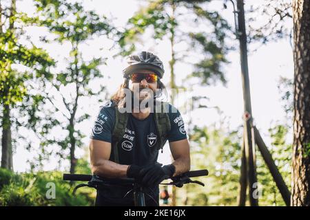 Lächelnder Radler mit Helm, der auf dem Fahrrad gelehnt ist Stockfoto