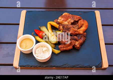 Gegrillte Rippchen mit Gemüse, Gewürzen und Saucen auf einem Steinteller in einem Holzrahmen. Stockfoto