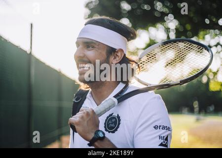 Glücklicher Mann mit Stirnband, der mit einem Tennisschläger davonschaut Stockfoto