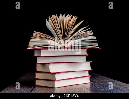 Stapel rot gebundener Papierbücher auf einem Holztisch. Auf dem Stapel befindet sich ein offenes Buch. Stockfoto