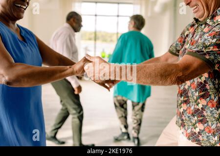 Mittelteil eines glücklichen älteren Paares, das sich beim Tanzen im Unterricht die Hände hält Stockfoto