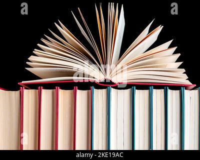 Nahaufnahme eines offenen Buches auf einer Reihe gebundener Bücher vor dunklem Hintergrund. Papierbücher. Stockfoto