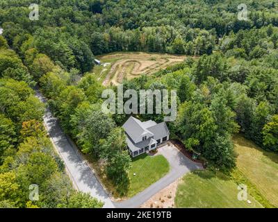 Eine Luftaufnahme eines Waldes mit einem modernen Custom New England Kolonialhaus Stockfoto