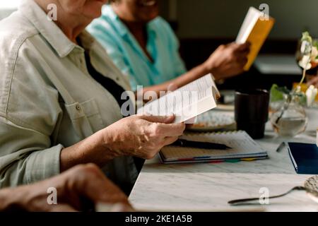 Mittelteil der älteren Frau beim Lesen des Buches, während sie von einer Freundin im Café sitzt Stockfoto