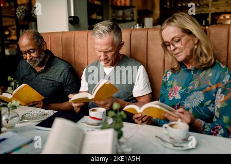 Ältere Männer und Frauen, die Bücher lesen, während sie im Café sitzen Stockfoto