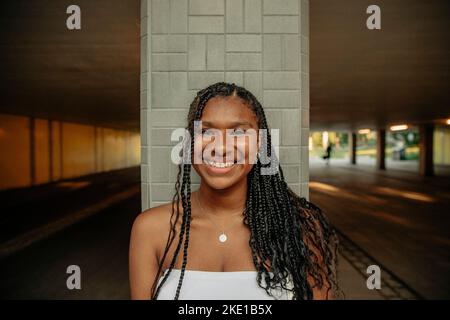 Porträt eines glücklichen Teenagers mit geflochtenen Haaren, die gegen die Säule stehen Stockfoto