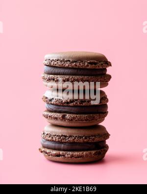 Hausgemachte Schoko-Makronen mit dunkler Schokoladenfüllung minimalistisch auf einem rosafarbenen Tisch. Nahaufnahme mit einem Stapel köstlicher Kakaomakronen. Stockfoto