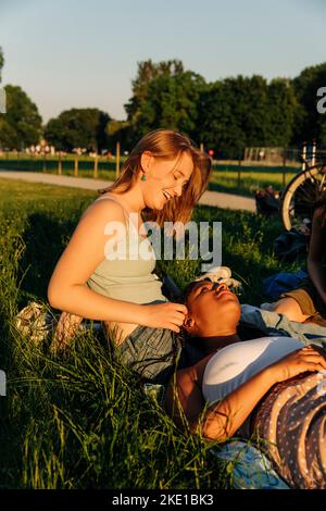 Lächelndes Teenager-Mädchen, das mit einer Freundin spricht, die auf dem Schoß im Park liegt Stockfoto