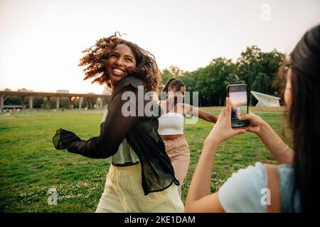 Teenager-Mädchen fotografieren glückliche weibliche Freunde tanzen im Park Stockfoto