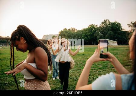 Teenager-Mädchen fotografieren weibliche Freunde genießen Tanz im Park bei Sonnenuntergang Stockfoto