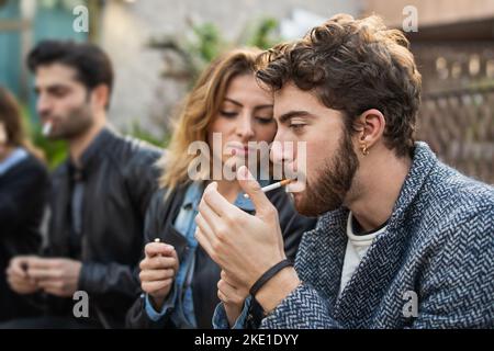 Gruppe von Freunden, die Zigaretten zünden und gemeinsam rauchen sitzen auf einer Bank im Freien - schlechte Gewohnheiten und sucht Menschen Lifestyle-Konzept Stockfoto